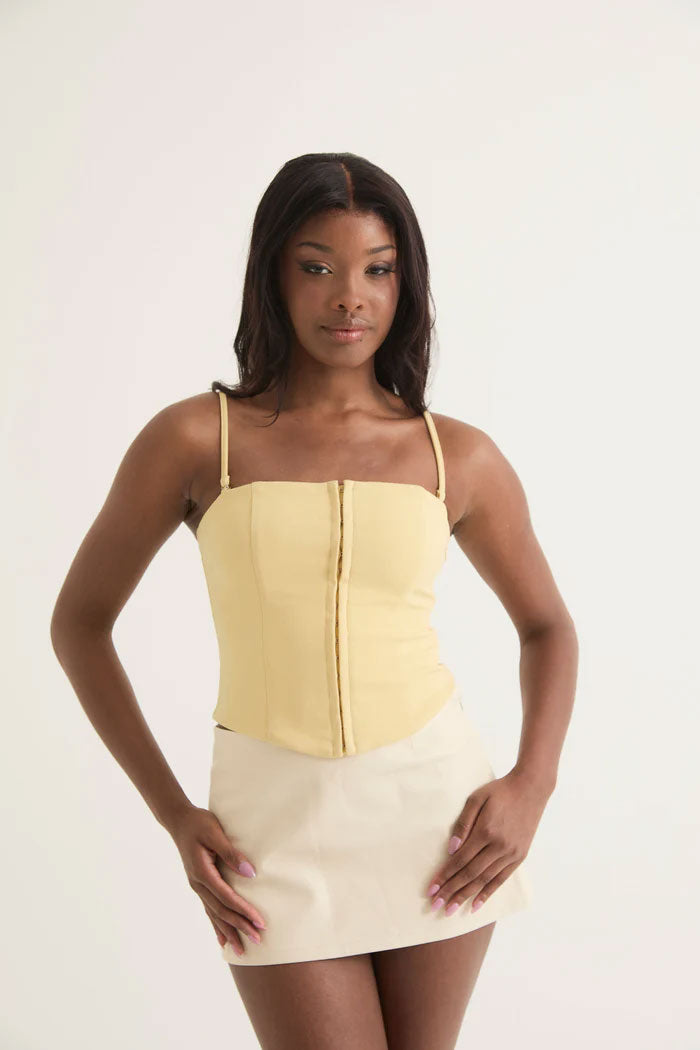 Woman in a light yellow spaghetti strap corset top with a cream mini skirt